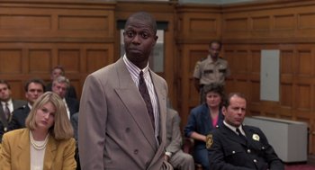 Movie still from “Striking Distance” (1993), directed by Rowdy Herrington – A man wearing a suit and tie in a courtroom; Medium shot, Low angle