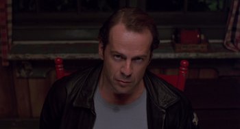 Movie still from “Striking Distance” (1993), directed by Rowdy Herrington – A person sitting in a chair wearing a leather jacket; Close Up shot, Over the shoulder angle