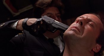 Movie still from “Striking Distance” (1993), directed by Rowdy Herrington – A man in a black suit holding a gun pointed at another man in a black suit holding a gun; Close Up shot, Low angle