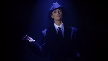 Movie still from “Striptease” (1996), directed by Andrew Bergman – A man in a suit and a hat is holding a gun; Medium shot, Low angle