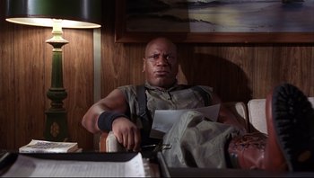 Movie still from “Striptease” (1996), directed by Andrew Bergman – A man sitting at a table with papers in front of him; Medium shot, Low angle