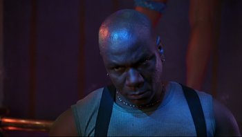 Movie still from “Striptease” (1996), directed by Andrew Bergman – A bald man with a black shirt is looking at the camera; Close Up shot, Low angle