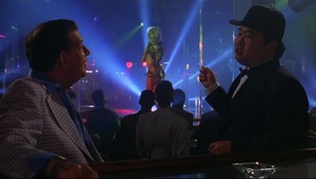 Movie still from “Striptease” (1996), directed by Andrew Bergman – Two men in suits and hats are talking in front of an audience; Medium shot, Over the shoulder angle