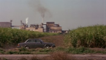 Movie still from “Striptease” (1996), directed by Andrew Bergman – A car driving down a dirt road near a factory; Extreme Wide shot, Low angle