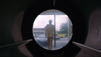 Movie still from “Striptease” (1996), directed by Andrew Bergman – A man in a hat is looking through a round window; Wide shot, Low angle