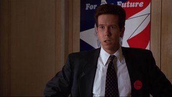 Movie still from “Striptease” (1996), directed by Andrew Bergman – A man in a suit and tie standing in front of an american flag; Close Up shot, Low angle