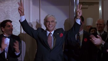 Movie still from “Striptease” (1996), directed by Andrew Bergman – A man in a suit and tie holding up a peace sign with both hands; Medium shot, Low angle
