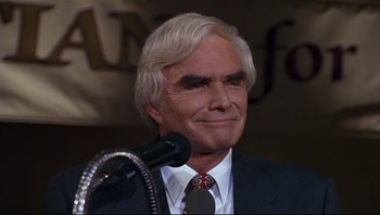 Movie still from “Striptease” (1996), directed by Andrew Bergman – An older man in a suit is speaking into a microphone; Close Up shot, High angle