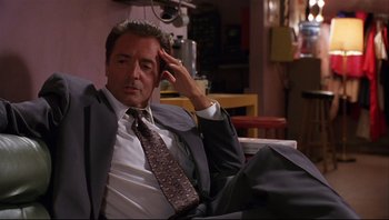 Movie still from “Striptease” (1996), directed by Andrew Bergman – A man in a suit and tie sitting on a couch; Medium shot, Low angle