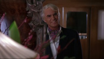 Movie still from “Striptease” (1996), directed by Andrew Bergman – A man in a suit and tie smiling for the camera; Close Up shot, Over the shoulder angle