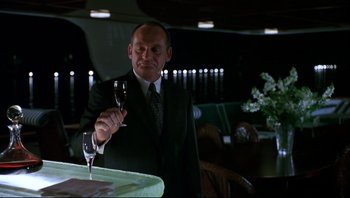 Movie still from “Striptease” (1996), directed by Andrew Bergman – A man in a suit and tie holding a glass of wine; Medium shot, Low angle