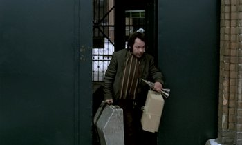 Movie still from “Stroszek” (1977), directed by Werner Herzog – A man holding a suitcase and a box in a doorway; Medium shot, High angle