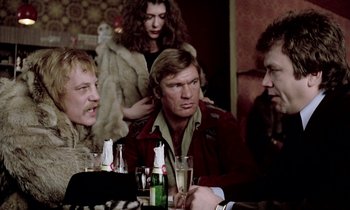 Movie still from “Stroszek” (1977), directed by Werner Herzog – A group of people sitting at a table with drinks; Medium shot, Over the shoulder angle