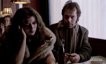 Movie still from “Stroszek” (1977), directed by Werner Herzog – A man and a woman sitting in front of a wine bottle; Medium shot, Low angle