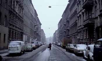 Movie still from “Stroszek” (1977), directed by Werner Herzog – A person riding a motorcycle down a street lined with parked cars; Extreme Wide shot, High angle