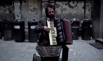 Movie still from “Stroszek” (1977), directed by Werner Herzog – A man playing an accordion on the street; Medium shot, Overhead angle