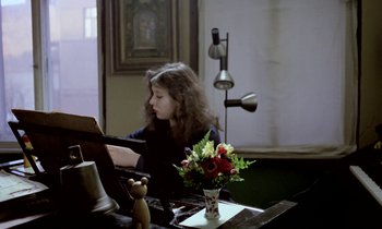 Movie still from “Stroszek” (1977), directed by Werner Herzog – A young girl sitting at a table playing a piano; Medium shot, High angle