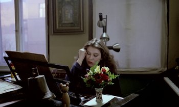 Movie still from “Stroszek” (1977), directed by Werner Herzog – A woman sitting at a table in front of a vase of flowers; Medium shot, High angle