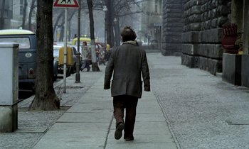 Movie still from “Stroszek” (1977), directed by Werner Herzog – A man walking down the sidewalk of a street; Wide shot, Over the shoulder angle