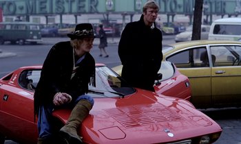 Movie still from “Stroszek” (1977), directed by Werner Herzog – Two people sitting on the hood of a red car; Wide shot, Low angle