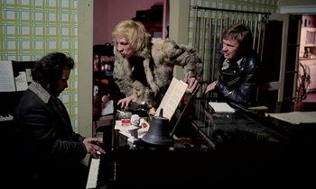 Movie still from “Stroszek” (1977), directed by Werner Herzog – A group of people sitting at a table with a piano; Medium shot, High angle