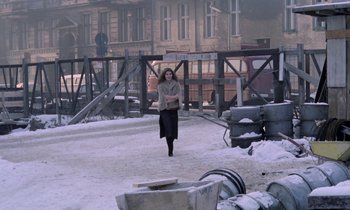 Movie still from “Stroszek” (1977), directed by Werner Herzog – A woman is walking in the snow near a building; Wide shot, Over the shoulder angle