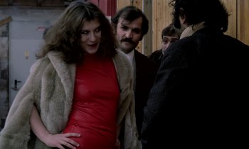 Movie still from “Stroszek” (1977), directed by Werner Herzog – A woman in a red dress standing next to two men; Medium shot, Over the shoulder angle
