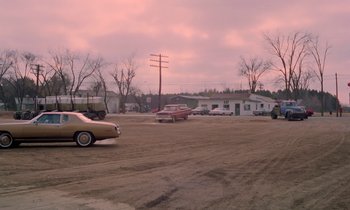 Movie still from “Stroszek” (1977), directed by Werner Herzog – Cars are parked in a parking lot in a rural area; Extreme Wide shot, High angle