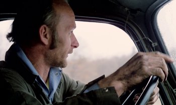 Movie still from “Stroszek” (1977), directed by Werner Herzog – A man sitting in the drivers seat of a car; Close Up shot, Low angle