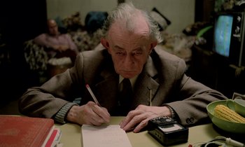 Movie still from “Stroszek” (1977), directed by Werner Herzog – An older man writing on a piece of paper; Medium shot, High angle