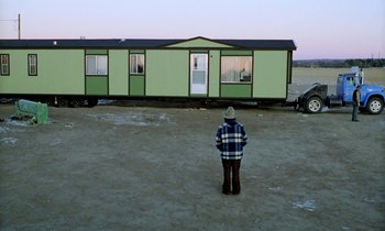 Movie still from “Stroszek” (1977), directed by Werner Herzog – A man standing in front of a green trailer; Extreme Wide shot, Low angle