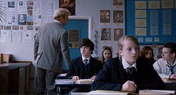 Movie still from “Submarine” (2010), directed by Richard Ayoade – A group of people sitting at a desk in a room; Medium shot, Over the shoulder angle