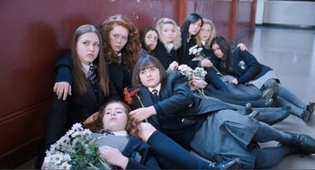 Movie still from “Submarine” (2010), directed by Richard Ayoade – A group of young women sitting next to each other holding flowers; Wide shot, High angle
