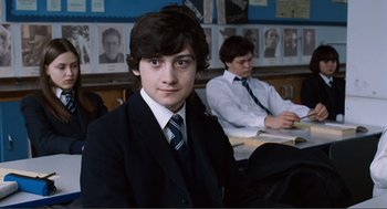 Movie still from “Submarine” (2010), directed by Richard Ayoade – A boy in a suit sitting in front of another boy in a tie; Medium shot, Over the shoulder angle