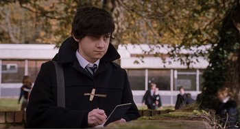 Movie still from “Submarine” (2010), directed by Richard Ayoade – A young man writing on a piece of paper; Medium shot, Over the shoulder angle
