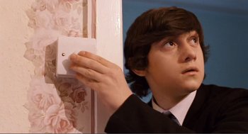 Movie still from “Submarine” (2010), directed by Richard Ayoade – A young man in a suit and tie holding on to an electrical outlet; Close Up shot, High angle