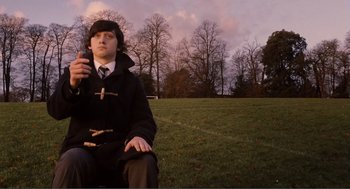 Movie still from “Submarine” (2010), directed by Richard Ayoade – A man sitting on the grass holding a cell phone in his hand; Medium shot, Low angle