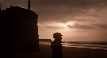 Movie still from “Submarine” (2010), directed by Richard Ayoade – A man standing on the beach near the water; Extreme Wide shot, Low angle