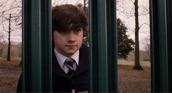 Movie still from “Submarine” (2010), directed by Richard Ayoade – A young man in a suit and tie looking through a fence; Medium shot, Low angle