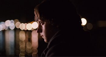 Movie still from “Submarine” (2010), directed by Richard Ayoade – A young man is standing in front of a street light at night; Close Up shot, Over the shoulder angle