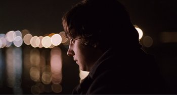 Movie still from “Submarine” (2010), directed by Richard Ayoade – A man with glasses is looking at the lights; Close Up shot, Over the shoulder angle