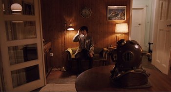 Movie still from “Submarine” (2010), directed by Richard Ayoade – A man sitting on a chair in a living room; Wide shot, High angle