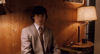 Movie still from “Submarine” (2010), directed by Richard Ayoade – A young man in a suit and tie in front of a wooden wall; Medium shot, High angle