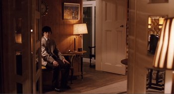 Movie still from “Submarine” (2010), directed by Richard Ayoade – A man sitting on a bench in a room; Wide shot, High angle