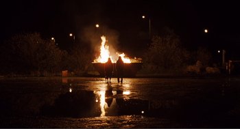 Movie still from “Submarine” (2010), directed by Richard Ayoade – Two people are standing in front of a fire at night; Extreme Wide shot, Low angle