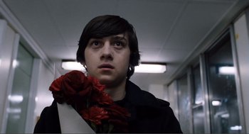 Movie still from “Submarine” (2010), directed by Richard Ayoade – A person holding a bouquet of roses in a room; Close Up shot, Low angle