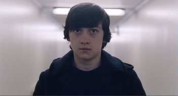 Movie still from “Submarine” (2010), directed by Richard Ayoade – A young man with long hair and blue eyes stares straight ahead; Close Up shot, High angle