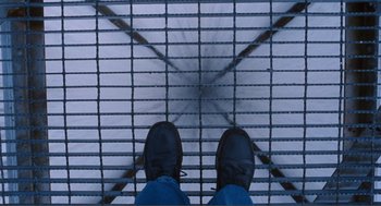 Movie still from “Submarine” (2010), directed by Richard Ayoade – A man standing on a metal grate next to a building; Wide shot, Overhead angle