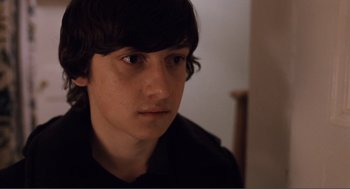 Movie still from “Submarine” (2010), directed by Richard Ayoade – A young man with long black hair stares into the camera; Close Up shot, High angle