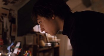 Movie still from “Submarine” (2010), directed by Richard Ayoade – A young man is looking into the distance in a dark room; Medium shot, Over the shoulder angle